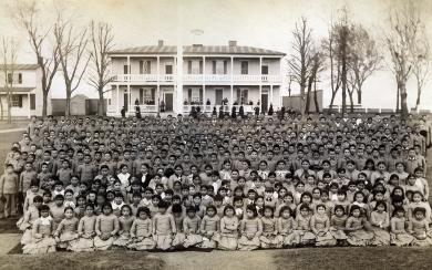 A large group of Native children in front of a boarding school.